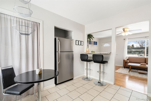 kitchen with ceiling fan, stainless steel fridge, light tile patterned floors, and a breakfast bar area