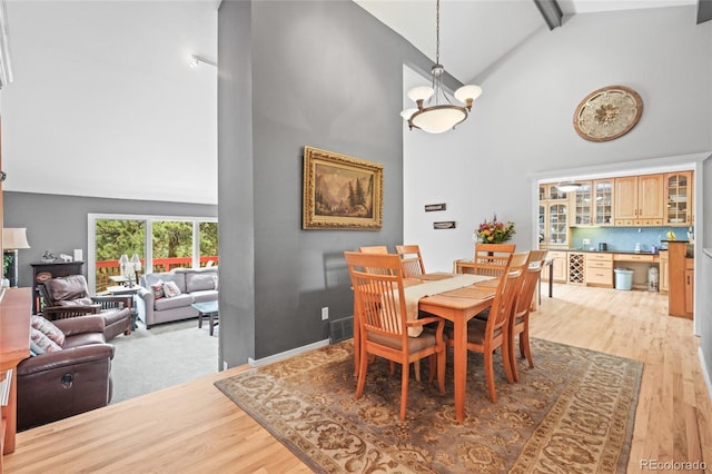 dining space with beamed ceiling, high vaulted ceiling, and light wood-type flooring