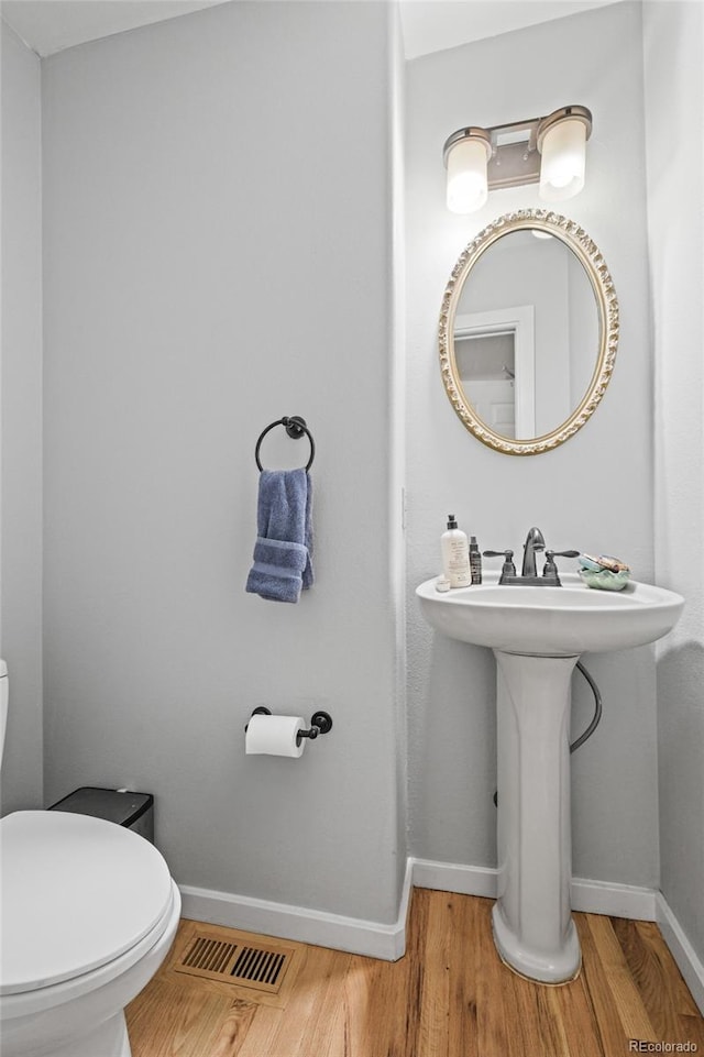 bathroom featuring a sink, toilet, baseboards, wood finished floors, and visible vents