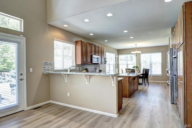 7329 Arco Iris Ln, Castle Pines, CO 80108 - kitchen with stainless steel microwave, a breakfast bar, a peninsula, light wood-type flooring, and recessed lighting