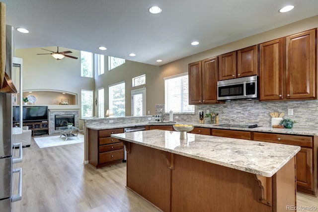 7329 Arco Iris Ln, Castle Pines, CO 80108 - kitchen featuring stainless steel microwave, a peninsula, black electric stovetop, a ceiling fan, and light stone counters