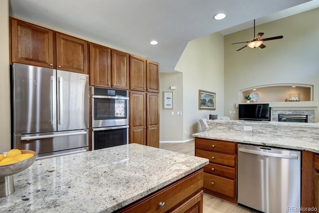 7329 Arco Iris Ln, Castle Pines, CO 80108 - kitchen featuring stainless steel appliances, light wood-type flooring, light stone countertops, brown cabinets, and vaulted ceiling