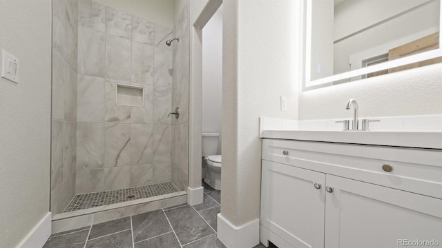 bathroom featuring toilet, tile patterned floors, tiled shower, and vanity