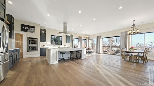 kitchen with light hardwood / wood-style floors, island exhaust hood, appliances with stainless steel finishes, hanging light fixtures, and a center island