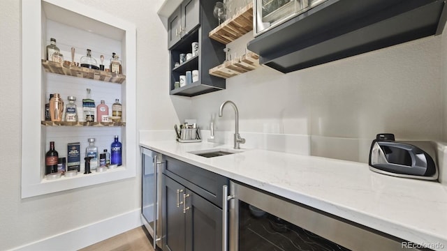 bar featuring light stone countertops, beverage cooler, and sink