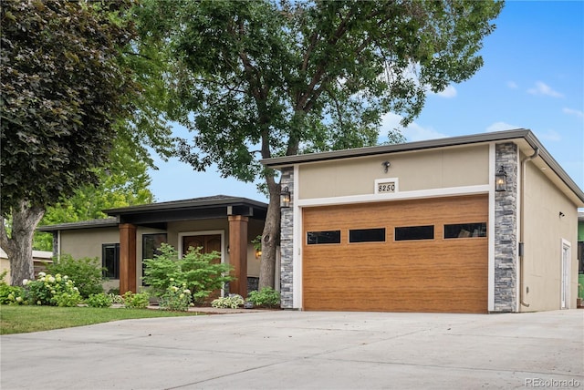 view of front of property featuring a garage, stone siding, driveway, and stucco siding