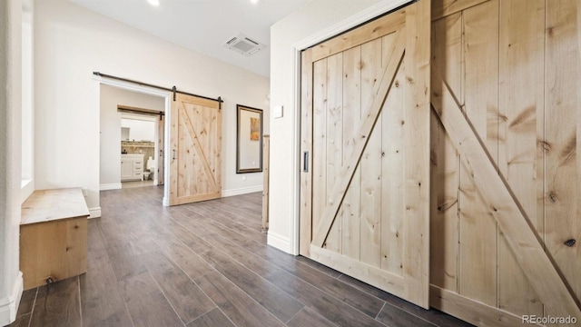 hallway with visible vents, dark wood finished floors, baseboards, and a barn door