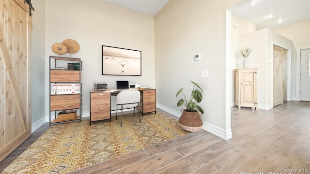 office area with a barn door, baseboards, and wood finished floors