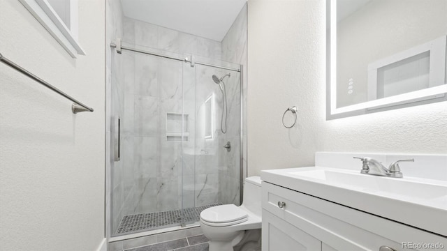 full bathroom featuring a marble finish shower, a textured wall, vanity, and toilet