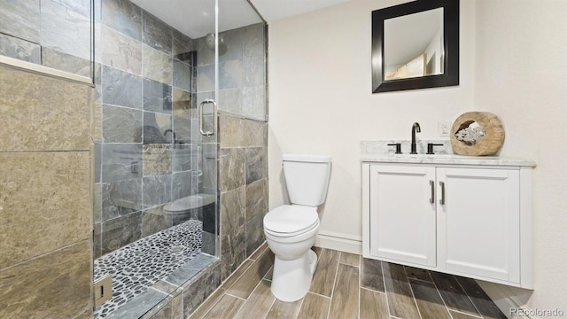 bathroom with wood tiled floor, a tile shower, vanity, and toilet