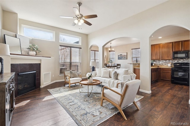 living room featuring dark wood-type flooring, a fireplace, baseboards, and ceiling fan with notable chandelier