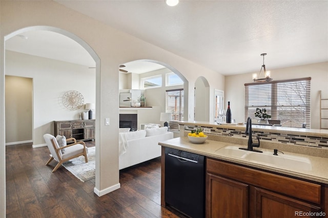 kitchen with black dishwasher, dark wood finished floors, a tiled fireplace, decorative backsplash, and a sink