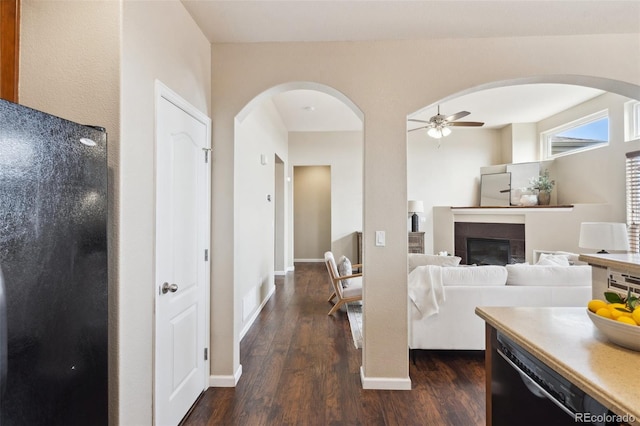 living area with arched walkways, ceiling fan, a fireplace, baseboards, and dark wood finished floors