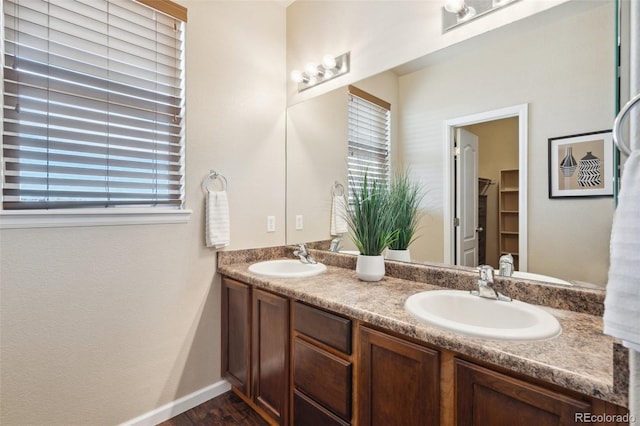 full bathroom with double vanity, baseboards, a sink, and wood finished floors