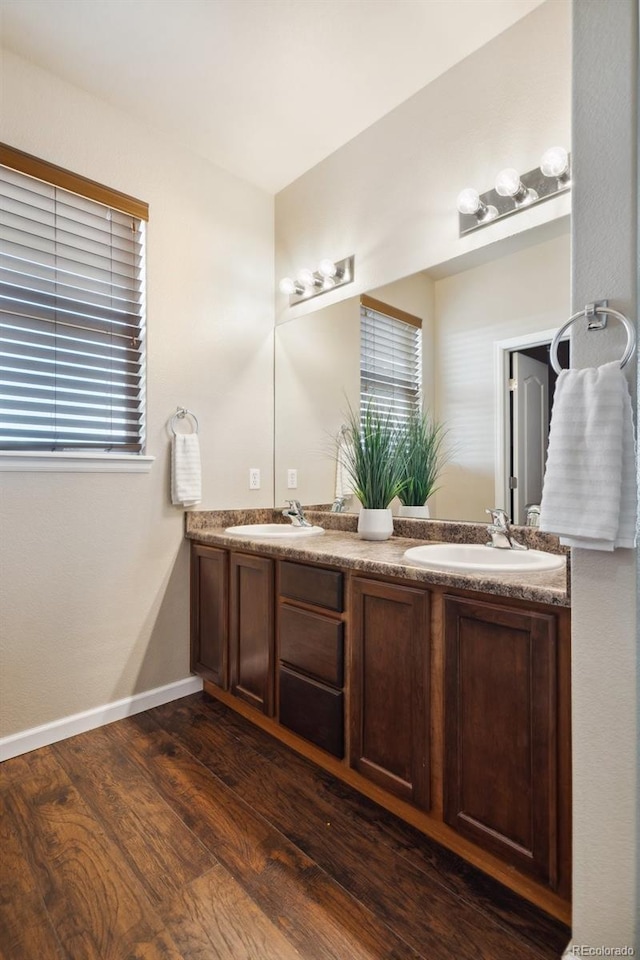 full bath with wood finished floors, a sink, baseboards, and double vanity