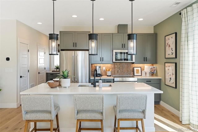 kitchen featuring gray cabinetry, sink, light hardwood / wood-style flooring, an island with sink, and stainless steel appliances