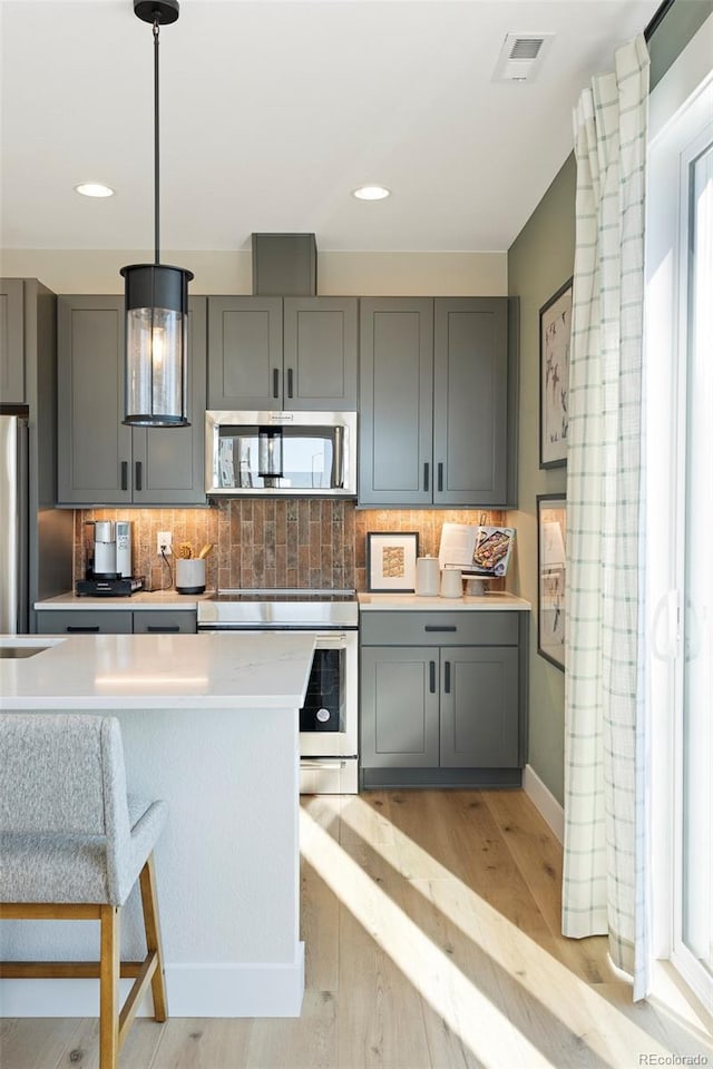 kitchen featuring stainless steel appliances, pendant lighting, gray cabinets, decorative backsplash, and light wood-type flooring