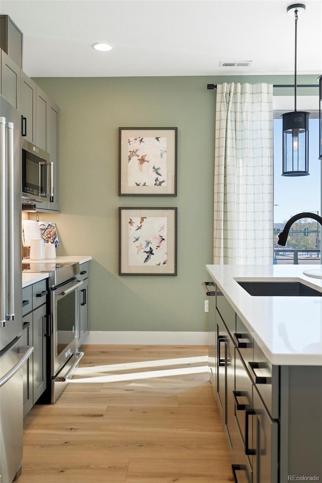 kitchen featuring gray cabinetry, sink, light wood-type flooring, appliances with stainless steel finishes, and decorative light fixtures