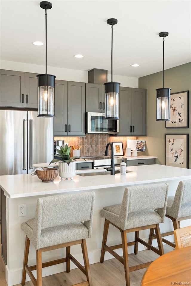 kitchen featuring gray cabinets, an island with sink, and appliances with stainless steel finishes