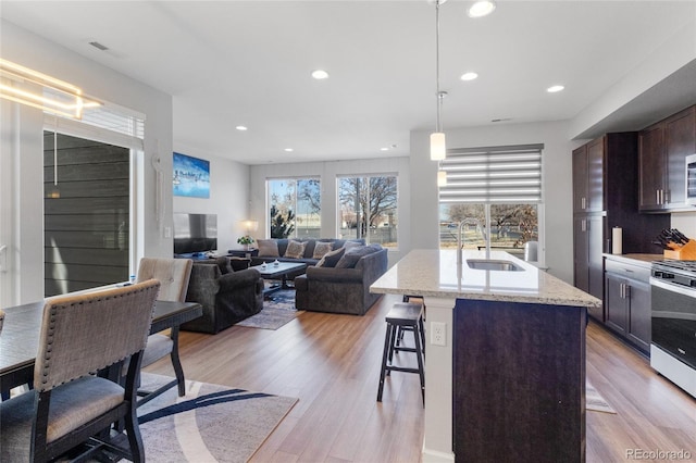 kitchen with light wood-style flooring, recessed lighting, a breakfast bar, a sink, and range with gas stovetop