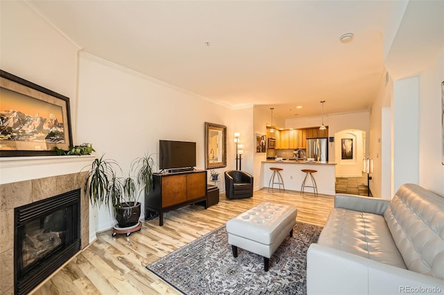 living room with a tile fireplace, crown molding, and light wood-type flooring