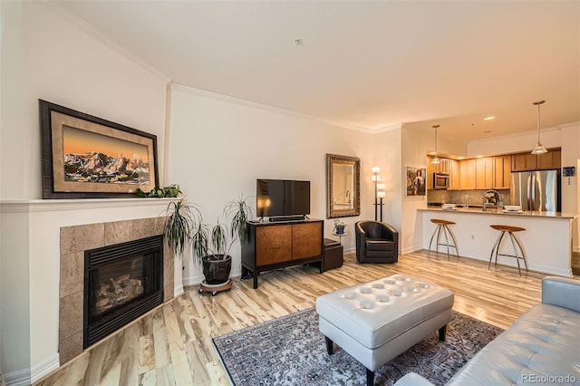 living room featuring a tiled fireplace, crown molding, and light hardwood / wood-style floors