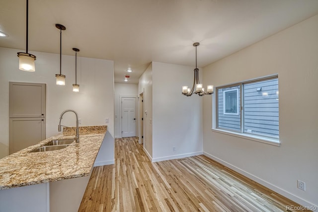 kitchen featuring a notable chandelier, light hardwood / wood-style floors, light stone countertops, sink, and decorative light fixtures