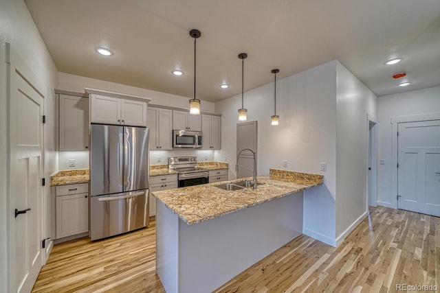 kitchen featuring stainless steel appliances, sink, hanging light fixtures, kitchen peninsula, and light wood-type flooring