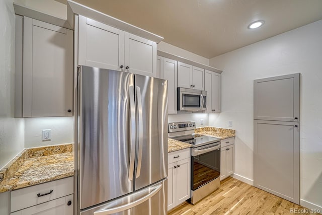 kitchen featuring white cabinets, stainless steel appliances, light stone counters, and light hardwood / wood-style floors