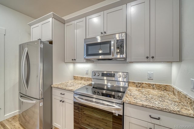 kitchen with light stone counters, white cabinets, light hardwood / wood-style floors, and stainless steel appliances