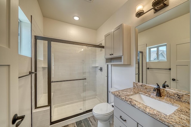 bathroom with wood-type flooring, a shower with door, toilet, and vanity