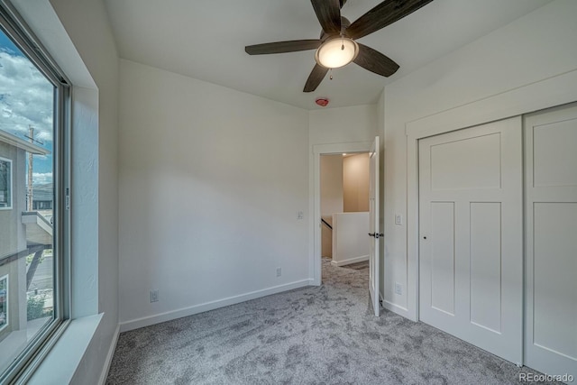 unfurnished bedroom with a closet, ceiling fan, light carpet, and multiple windows