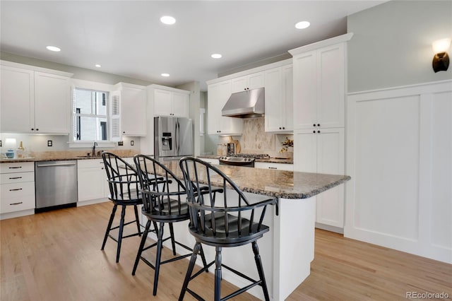 11776 Perry St, Westminster, CO 80031 - kitchen featuring a kitchen bar, under cabinet range hood, white cabinets, light wood finished floors, and appliances with stainless steel finishes