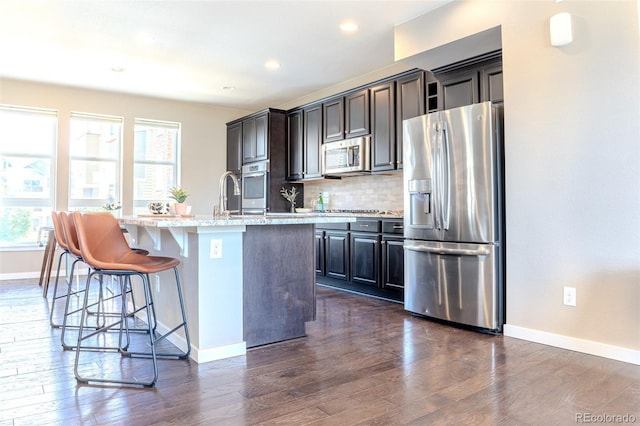 15738 E Broncos Pl, Englewood, CO 80112 - kitchen featuring stainless steel appliances, an island with sink, dark wood-style floors, decorative backsplash, and a breakfast bar area
