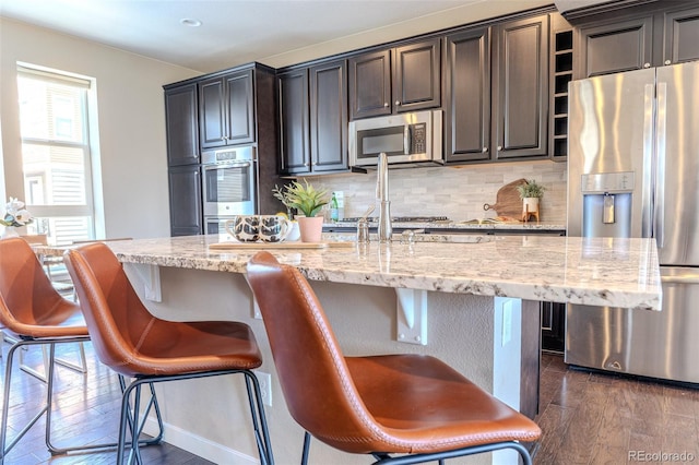15738 E Broncos Pl, Englewood, CO 80112 - kitchen with stainless steel appliances, dark wood-style floors, backsplash, light stone countertops, and a breakfast bar area