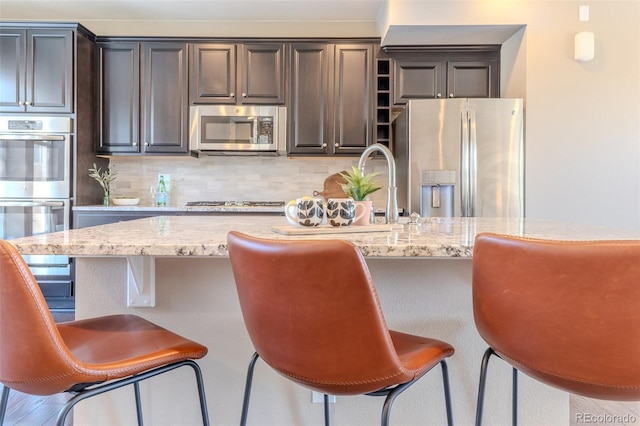 15738 E Broncos Pl, Englewood, CO 80112 - kitchen with appliances with stainless steel finishes, tasteful backsplash, light stone countertops, a breakfast bar, and dark brown cabinets