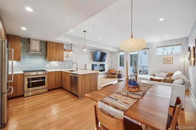 kitchen featuring light countertops, appliances with stainless steel finishes, open floor plan, a peninsula, and wall chimney exhaust hood