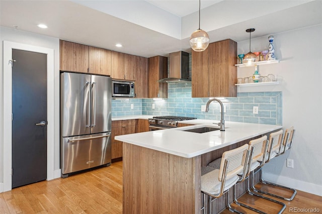 kitchen featuring a breakfast bar area, a peninsula, light countertops, wall chimney range hood, and high end appliances