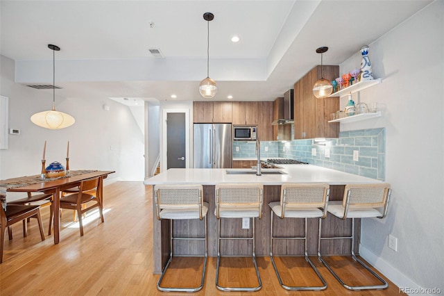 kitchen featuring kitchen peninsula, a kitchen breakfast bar, wall chimney range hood, and appliances with stainless steel finishes