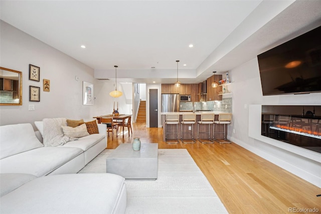 living area featuring recessed lighting, baseboards, stairs, light wood-style floors, and a glass covered fireplace