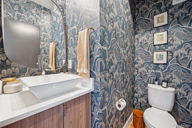 half bathroom featuring toilet, wallpapered walls, and vanity