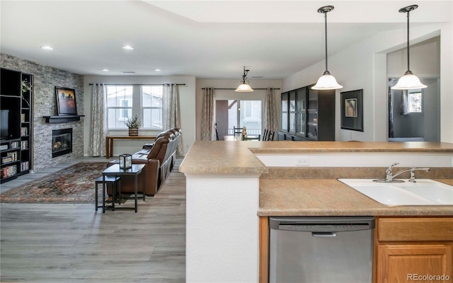 kitchen with sink, hanging light fixtures, dishwasher, a fireplace, and hardwood / wood-style floors