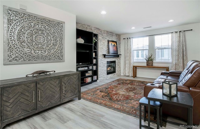 living room with hardwood / wood-style floors, a stone fireplace, and built in features