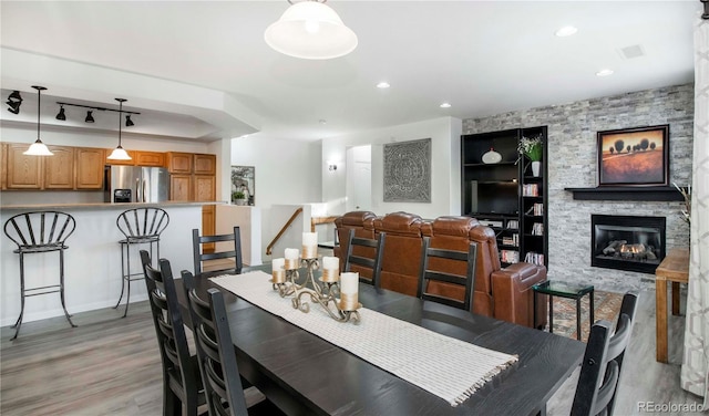 dining room with a stone fireplace, light hardwood / wood-style floors, and rail lighting