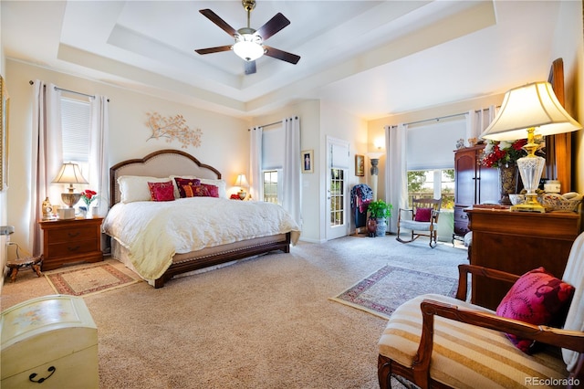 bedroom with ceiling fan, a tray ceiling, and light carpet