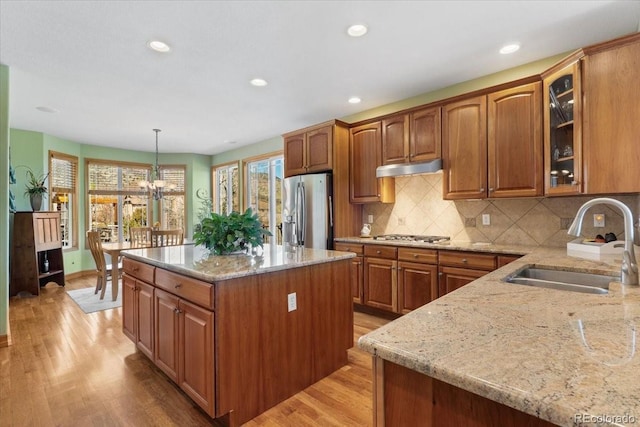 kitchen with light stone counters, a sink, brown cabinetry, and stainless steel fridge with ice dispenser