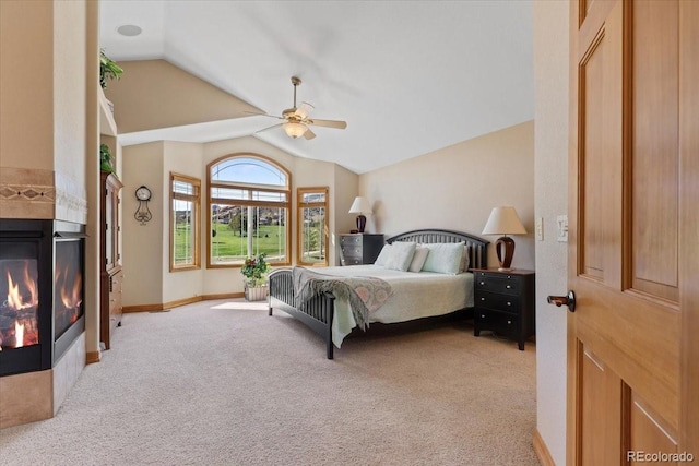 bedroom with a ceiling fan, a glass covered fireplace, lofted ceiling, and light carpet