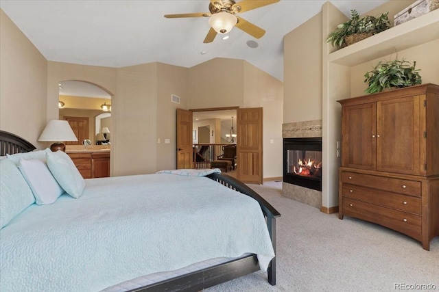 bedroom with a multi sided fireplace, visible vents, arched walkways, light carpet, and ensuite bath