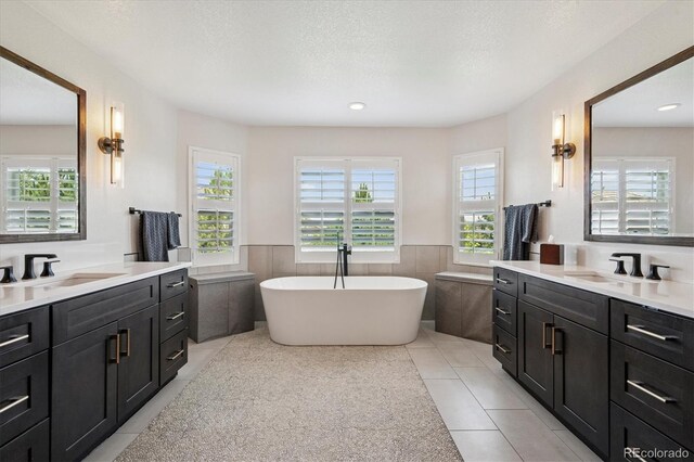 5665 Vistancia Ct, Parker, CO 80134 - bathroom featuring two vanities, tile patterned flooring, tile walls, a freestanding tub, and wainscoting