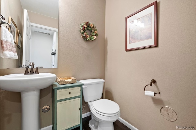 half bath with baseboards, visible vents, a sink, and toilet